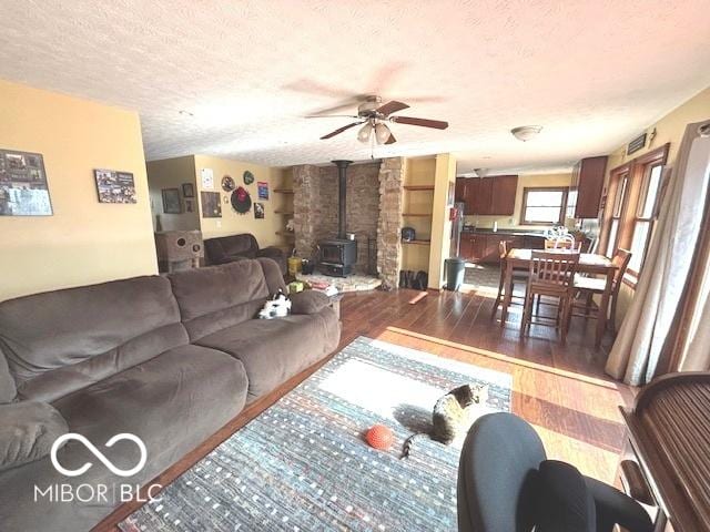 living room with a wood stove, ceiling fan, a textured ceiling, and wood finished floors