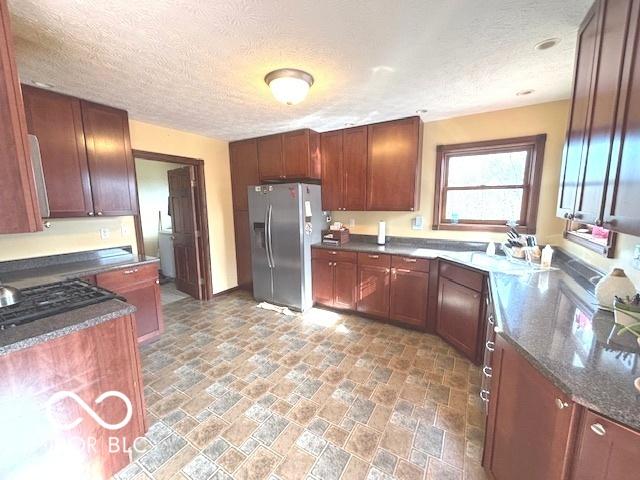 kitchen featuring a textured ceiling, stone finish floor, stainless steel refrigerator with ice dispenser, and dark stone countertops