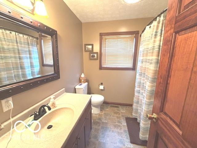 bathroom featuring a textured ceiling, toilet, vanity, baseboards, and stone finish floor