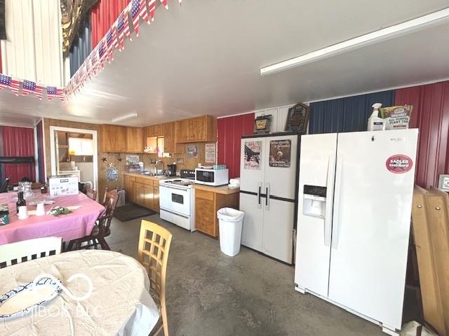 kitchen with white appliances, brown cabinetry, light countertops, concrete flooring, and wood walls