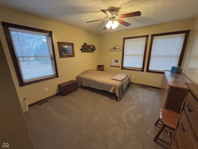 carpeted bedroom featuring a textured ceiling, baseboards, visible vents, and a ceiling fan