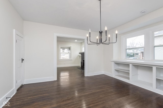 unfurnished dining area featuring an inviting chandelier, a brick fireplace, and dark hardwood / wood-style floors