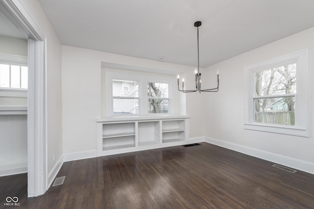 unfurnished dining area with plenty of natural light, dark wood-type flooring, and a notable chandelier