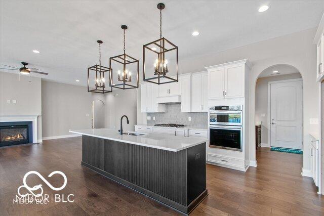 kitchen featuring arched walkways, appliances with stainless steel finishes, white cabinets, a sink, and a warm lit fireplace