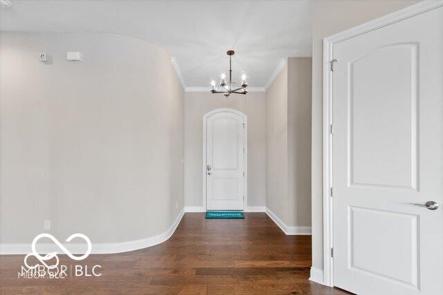 doorway featuring dark wood finished floors, a notable chandelier, crown molding, and baseboards