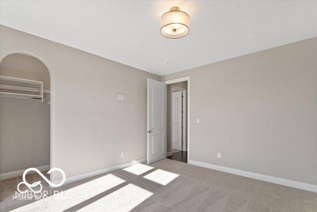 unfurnished bedroom featuring baseboards, arched walkways, a closet, and light colored carpet