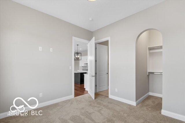 unfurnished bedroom featuring carpet floors, baseboards, and arched walkways