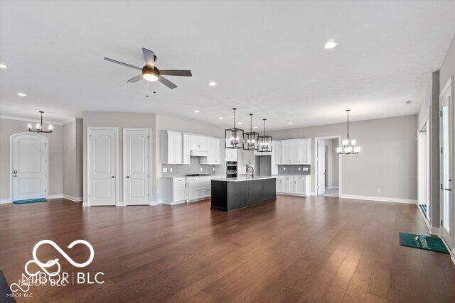 kitchen featuring ceiling fan with notable chandelier, white cabinets, open floor plan, light countertops, and an island with sink