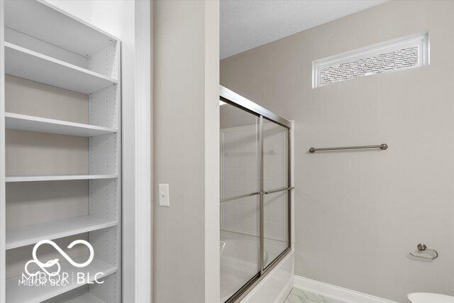 bathroom with combined bath / shower with glass door and baseboards