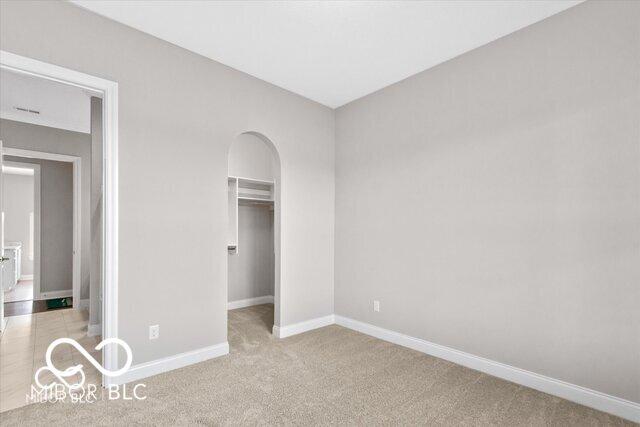 unfurnished bedroom featuring arched walkways, carpet flooring, baseboards, a spacious closet, and a closet