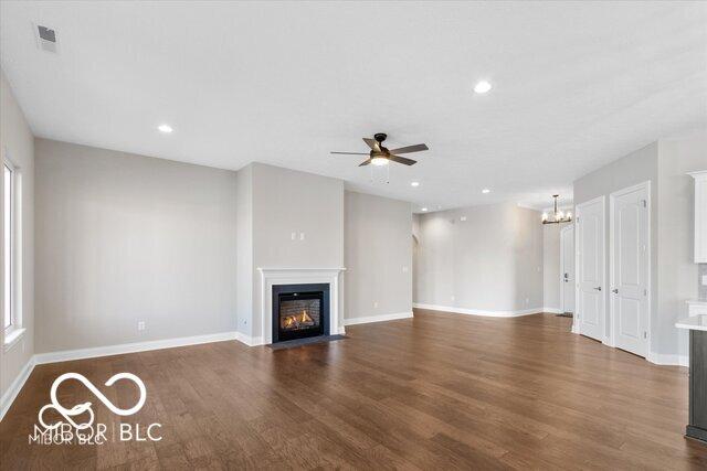 unfurnished living room featuring recessed lighting, a fireplace with flush hearth, wood finished floors, baseboards, and ceiling fan with notable chandelier