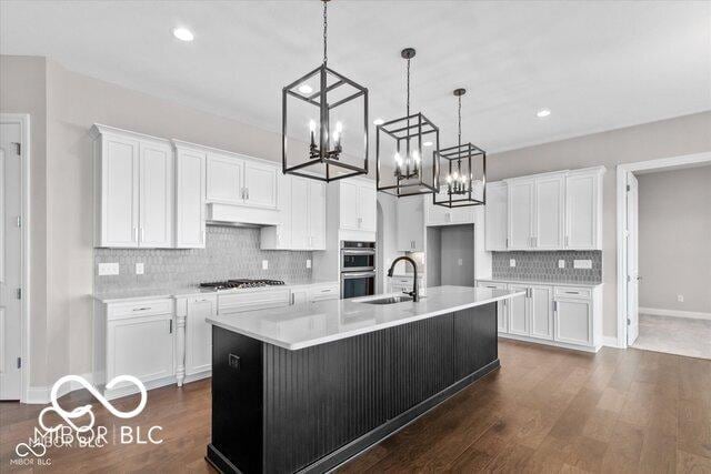 kitchen featuring light countertops, appliances with stainless steel finishes, white cabinetry, a sink, and an island with sink