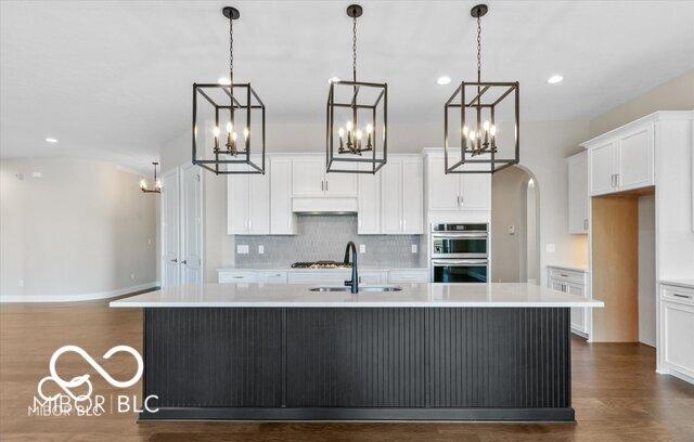 kitchen featuring arched walkways, stainless steel appliances, light countertops, a sink, and an island with sink