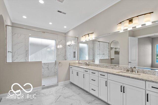 bathroom with a marble finish shower, visible vents, marble finish floor, crown molding, and a sink