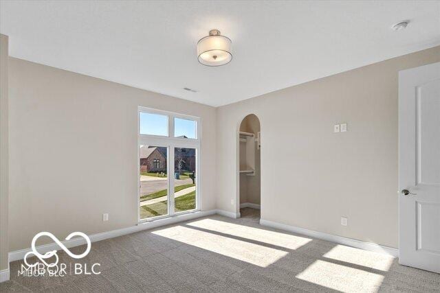 carpeted empty room with baseboards and arched walkways