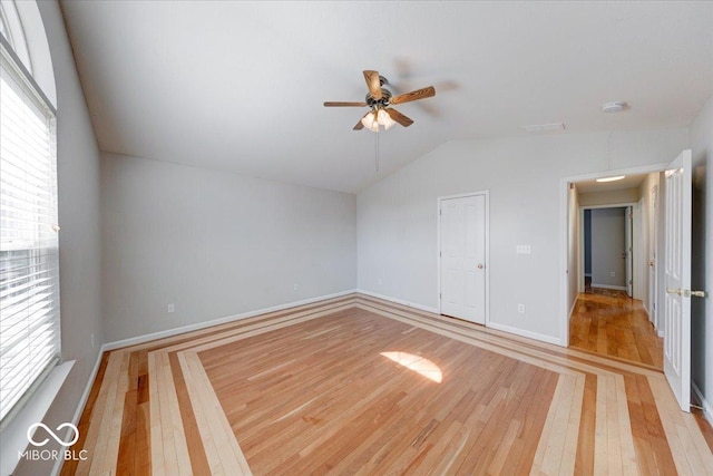 interior space featuring baseboards, light wood-style flooring, a ceiling fan, and vaulted ceiling