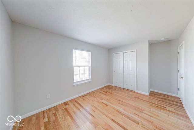 unfurnished bedroom featuring a closet, light wood-style flooring, a textured ceiling, and baseboards