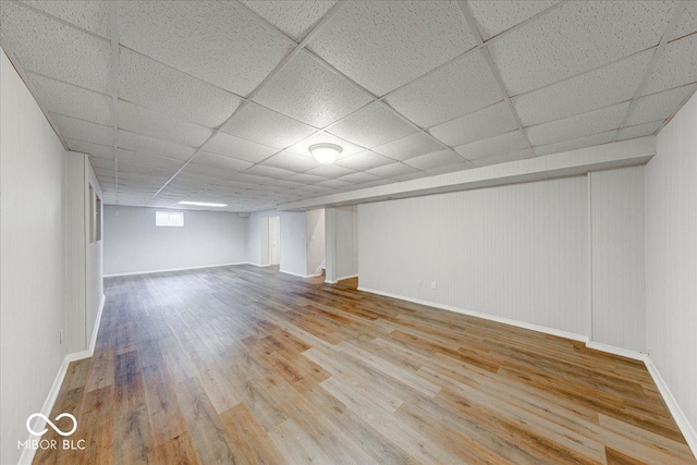 basement featuring a drop ceiling, baseboards, and wood finished floors