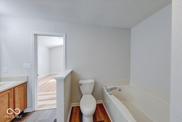 full bathroom with toilet, wood finished floors, baseboards, a bath, and vanity