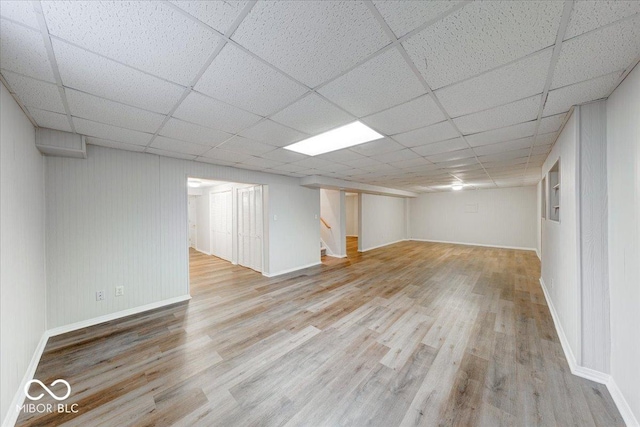 finished basement with stairway, wood finished floors, baseboards, and a drop ceiling