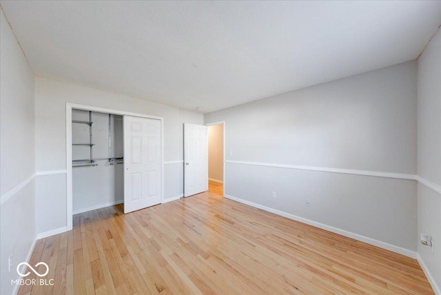 unfurnished bedroom featuring hardwood / wood-style floors, baseboards, and a closet