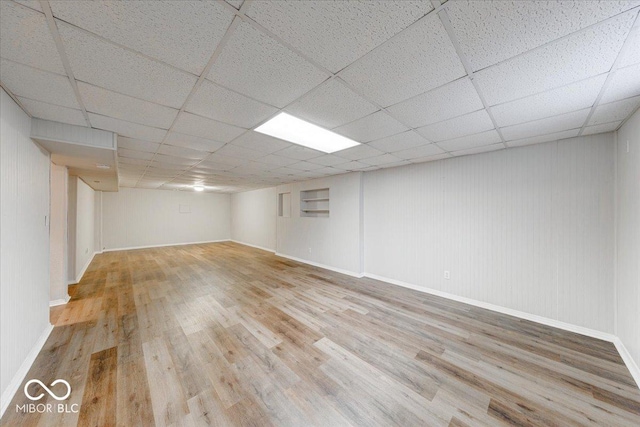 finished basement featuring baseboards, a paneled ceiling, and wood finished floors