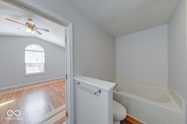 full bathroom featuring a bath, wood finished floors, a ceiling fan, lofted ceiling, and toilet