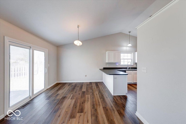 kitchen with dark wood finished floors, a peninsula, a sink, white cabinetry, and dark countertops