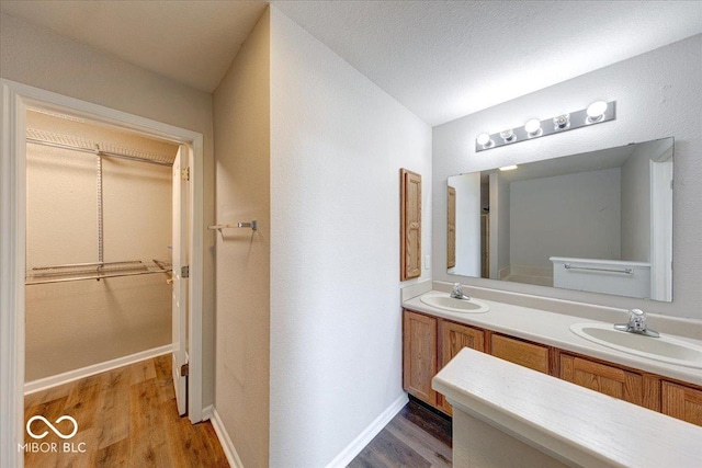 full bath featuring a sink, baseboards, wood finished floors, and double vanity