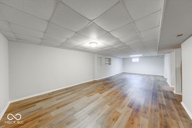 basement with wood finished floors, visible vents, a drop ceiling, and baseboards