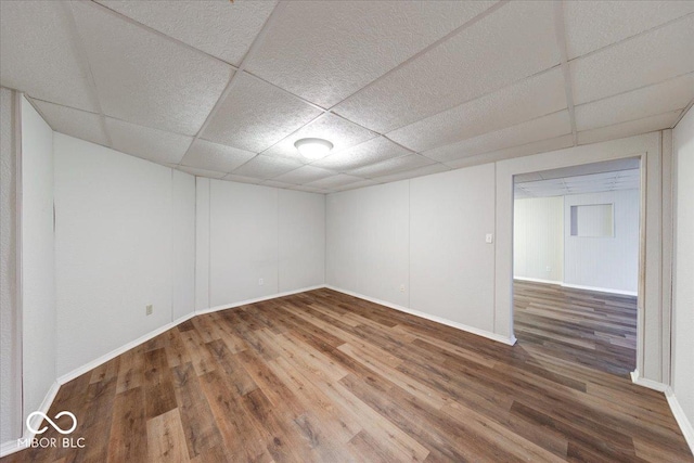 spare room with baseboards, a paneled ceiling, and wood finished floors