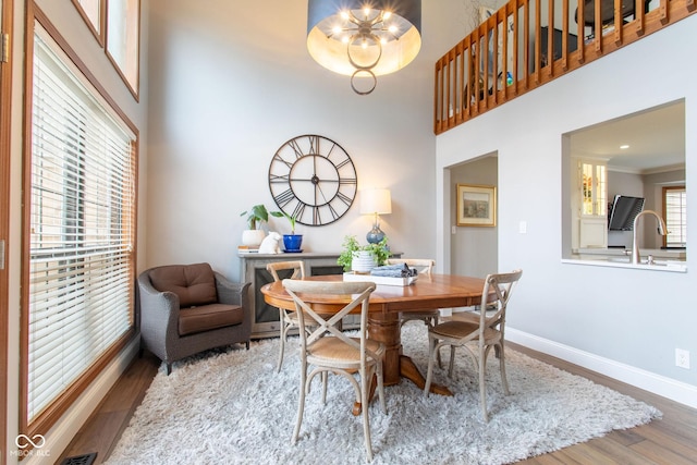 dining room with sink, crown molding, wood-type flooring, and a high ceiling