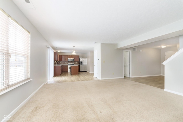 unfurnished living room featuring light carpet, a sink, visible vents, and baseboards