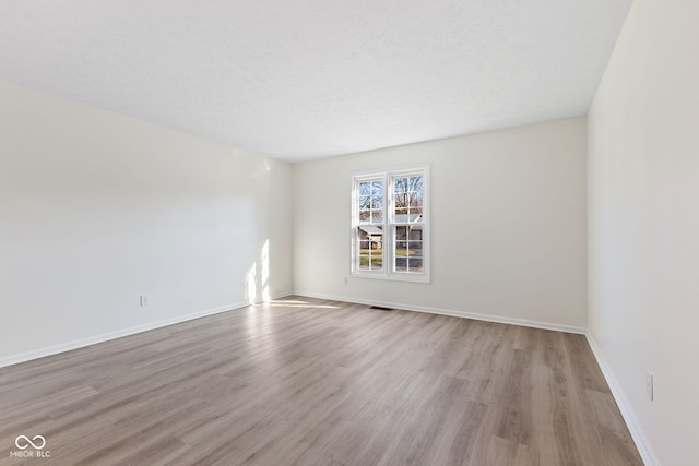 unfurnished room with a textured ceiling, baseboards, and wood finished floors