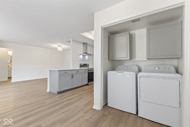 laundry room featuring visible vents, light wood-style floors, cabinet space, a textured ceiling, and separate washer and dryer