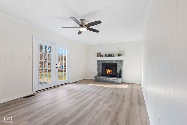 unfurnished living room with wood finished floors, visible vents, a fireplace, french doors, and a textured ceiling