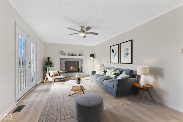 living area featuring visible vents, a textured ceiling, a stone fireplace, and light wood finished floors