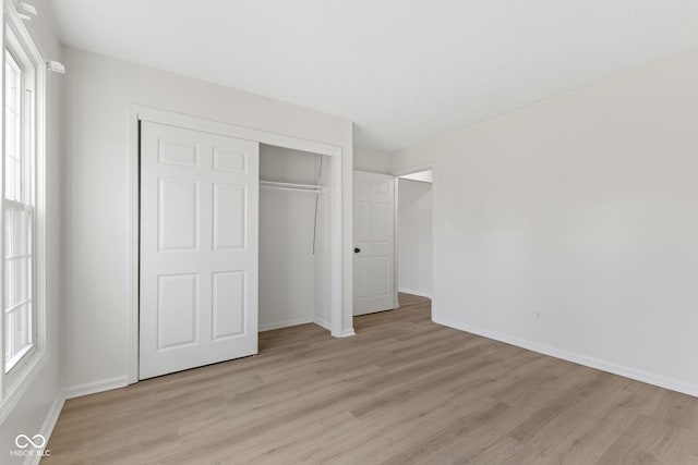 unfurnished bedroom with multiple windows, baseboards, a closet, and light wood finished floors