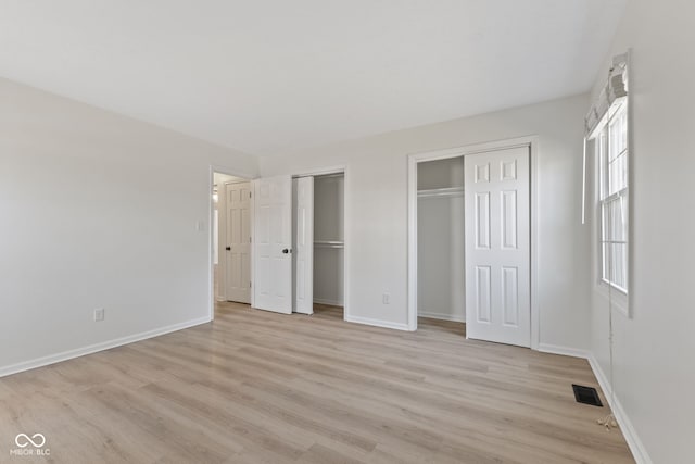 unfurnished bedroom featuring visible vents, multiple closets, light wood finished floors, and baseboards