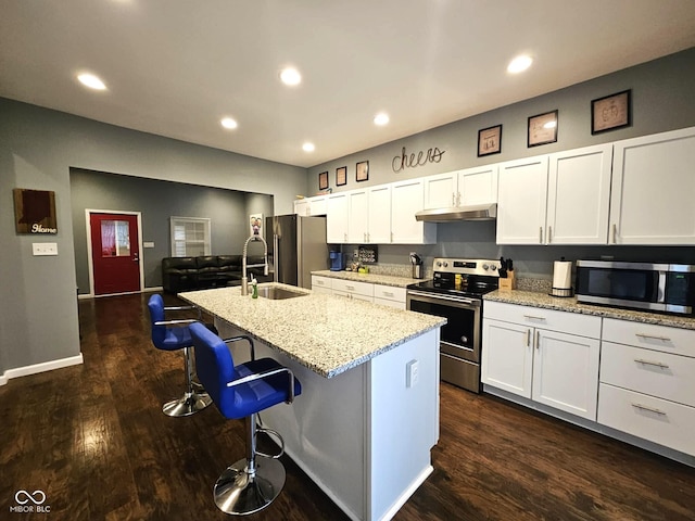 kitchen with appliances with stainless steel finishes, sink, white cabinets, a kitchen bar, and a center island with sink