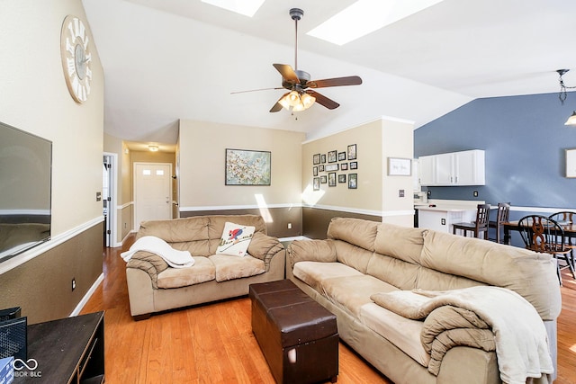 living room featuring light wood finished floors, vaulted ceiling with skylight, and a ceiling fan