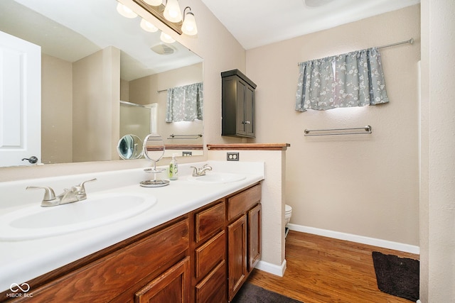 full bath featuring a stall shower, baseboards, a sink, and wood finished floors