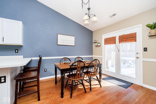 dining space with light wood finished floors, visible vents, vaulted ceiling, and a chandelier