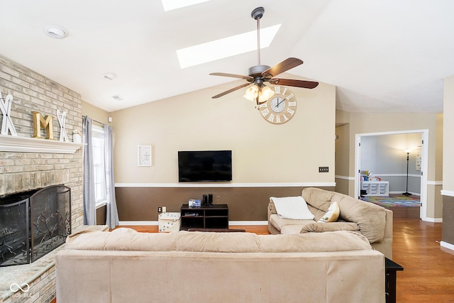 living room with lofted ceiling with skylight, a brick fireplace, baseboards, and wood finished floors