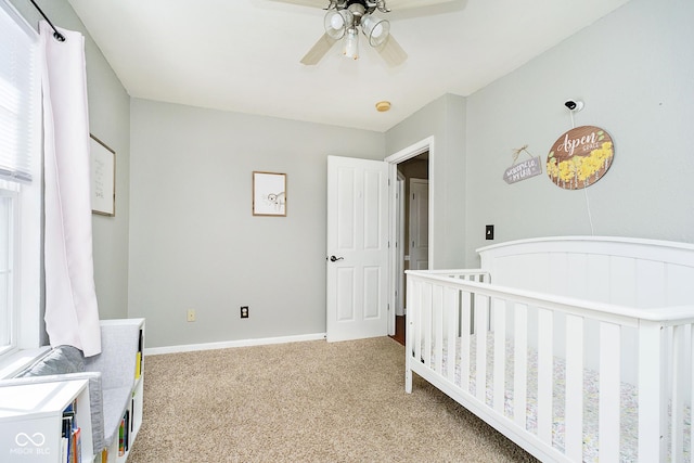 bedroom featuring light colored carpet, ceiling fan, a crib, and baseboards