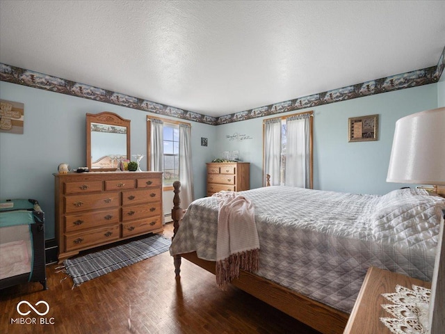 bedroom with a baseboard heating unit, dark wood-type flooring, and a textured ceiling