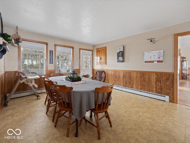 dining room with a baseboard heating unit, a textured ceiling, and wood walls