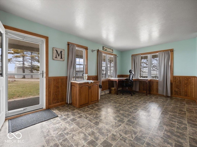 unfurnished office featuring plenty of natural light, baseboard heating, and wood walls