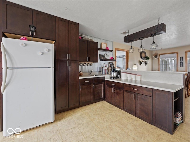 kitchen with pendant lighting, sink, white refrigerator, a textured ceiling, and kitchen peninsula