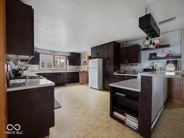 kitchen with sink, dark brown cabinetry, a textured ceiling, kitchen peninsula, and white fridge